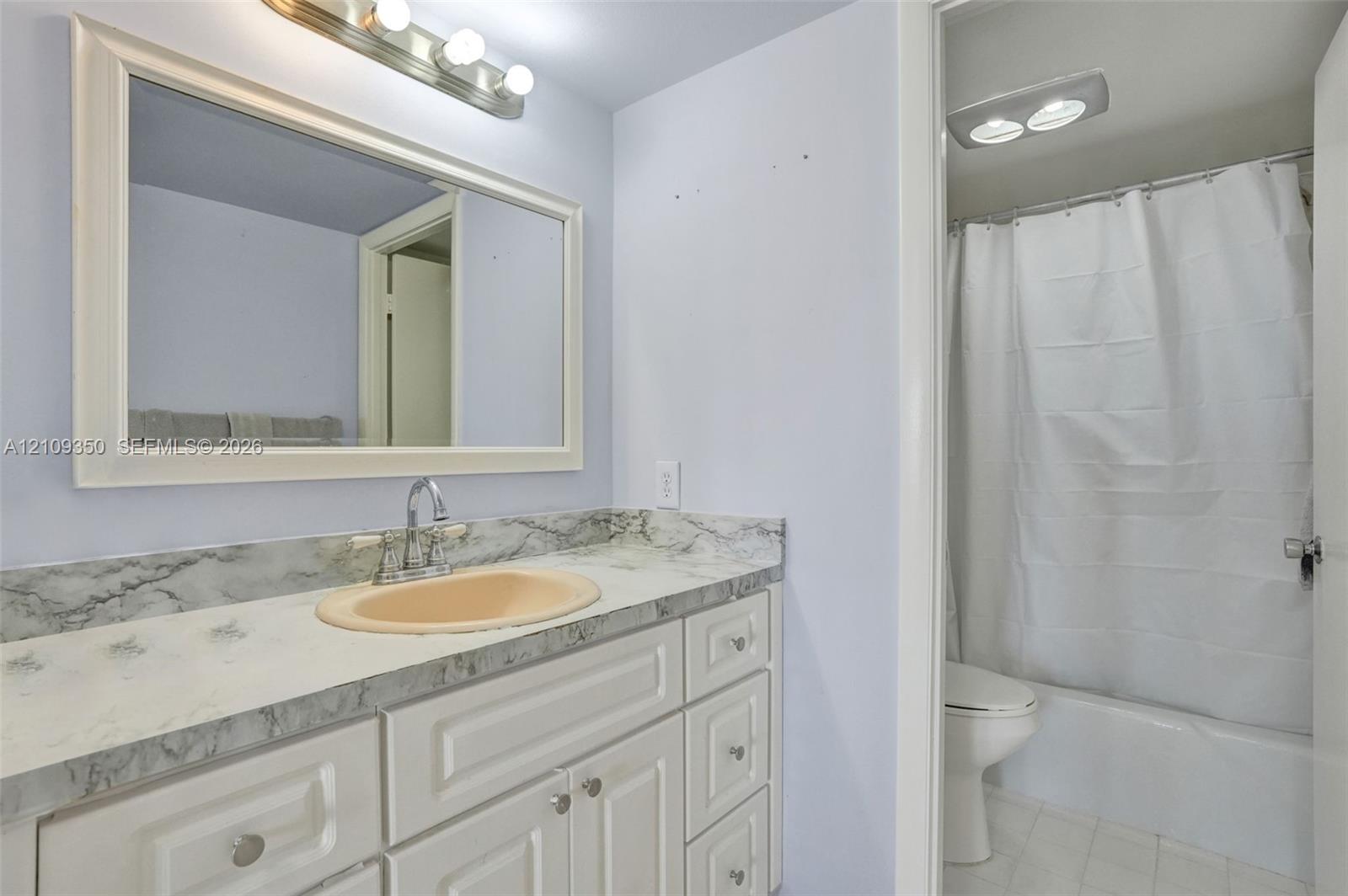 Bathroom featuring a vanity with white cabinetry, a stone-patterned countertop, an oval inset sink, a framed mirror with a four-light fixture, and a tub-shower combination
