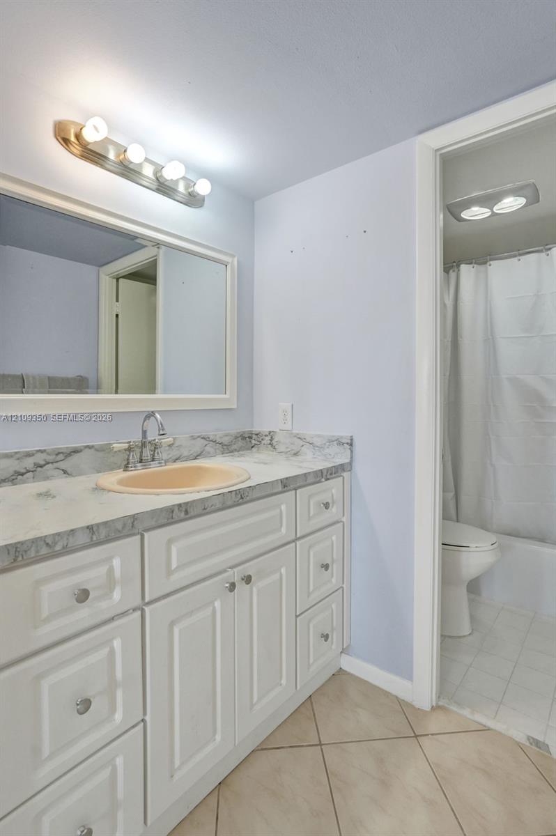 White cabinetry with paneled fronts, stone-finish countertop, oval undermount sink, wall-mounted mirror with white frame, and four-light vanity fixture
