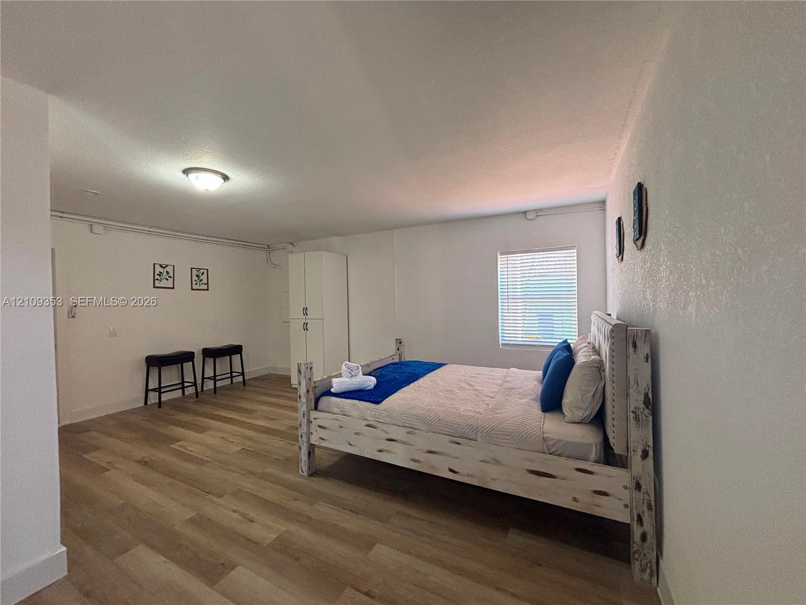Wood-finish flooring, white-finish built-in cabinetry, and a window with horizontal blinds