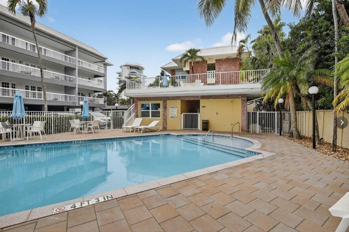 In-ground pool with stepped entry and paver patio surrounded by metal perimeter fencing and mature palm trees