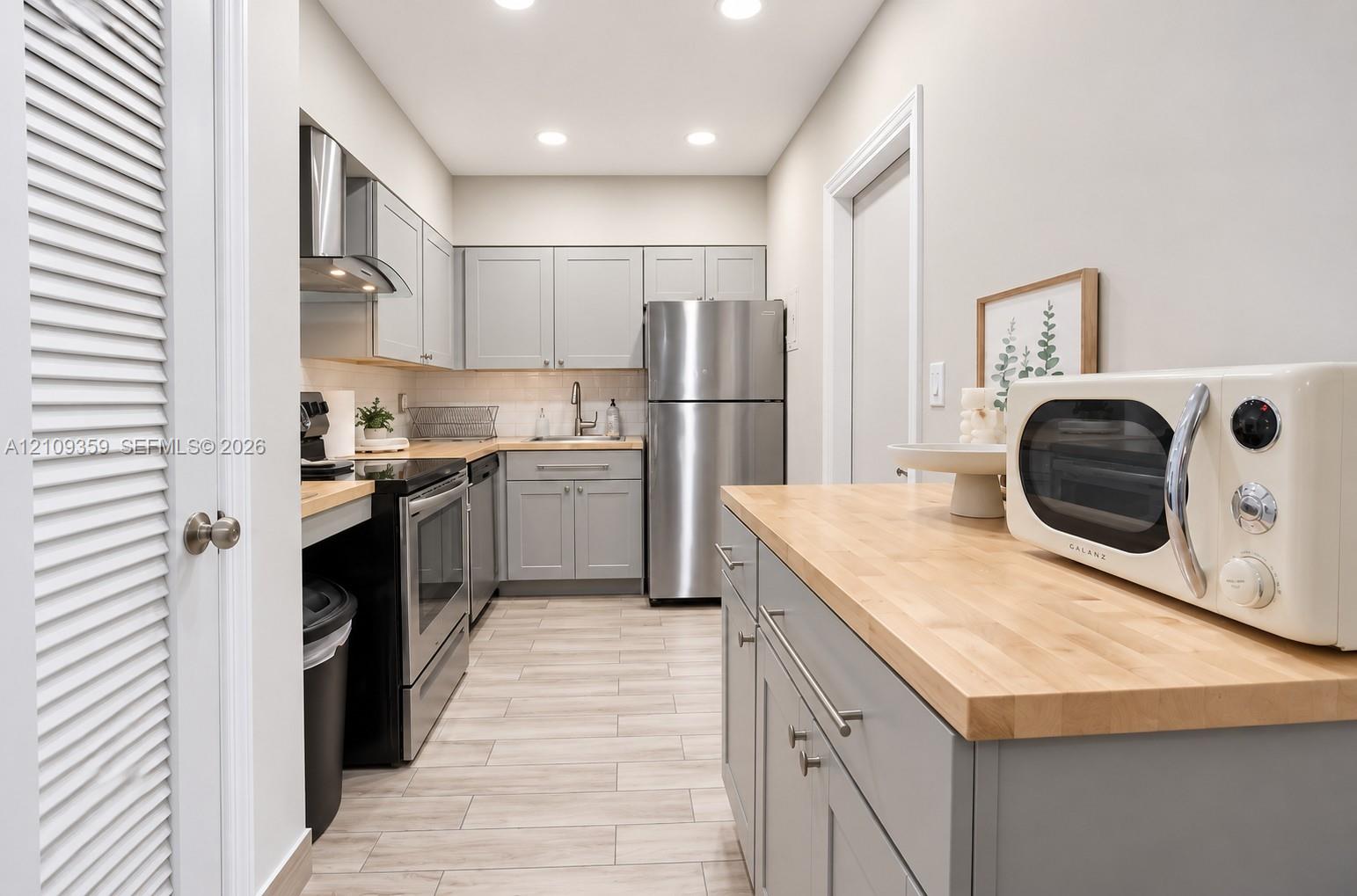 Kitchen featuring grey cabinetry, wood-finish countertops, stainless steel appliances, and wood-finish tile flooring Kitchen featuring grey cabinetry, wood-finish countertops, stainless steel appliances, and wood-finish tile flooring