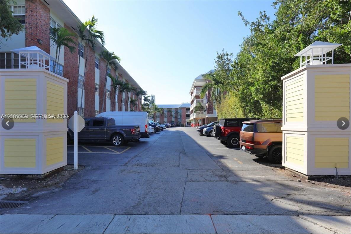 Gated entrance featuring decorative columns with roof caps, paved surface parking area, and mature landscaping