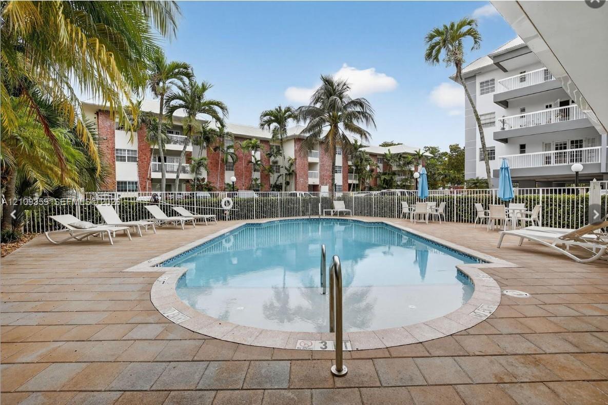 In-ground pool featuring a tiled deck, perimeter fencing, and mature palm trees