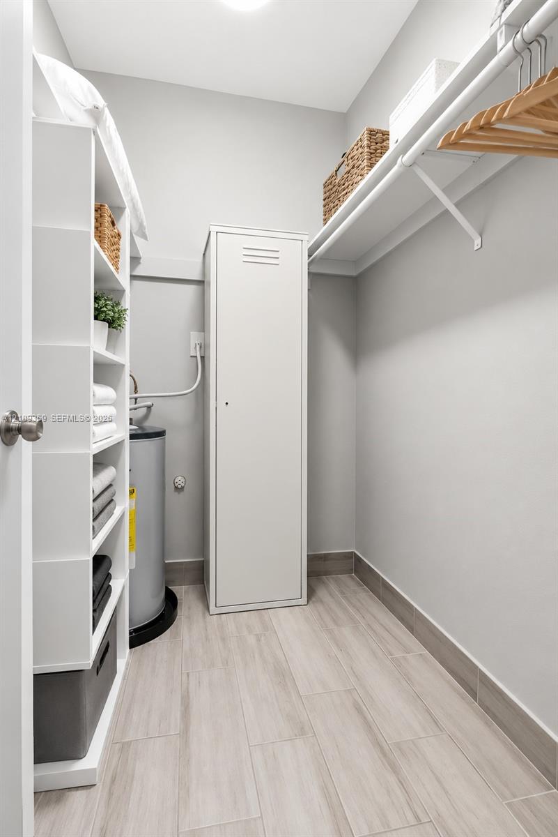 Storage space featuring built-in white shelving, a full-height metal cabinet, wall-mounted hanging rod, and wood-finish tile flooring