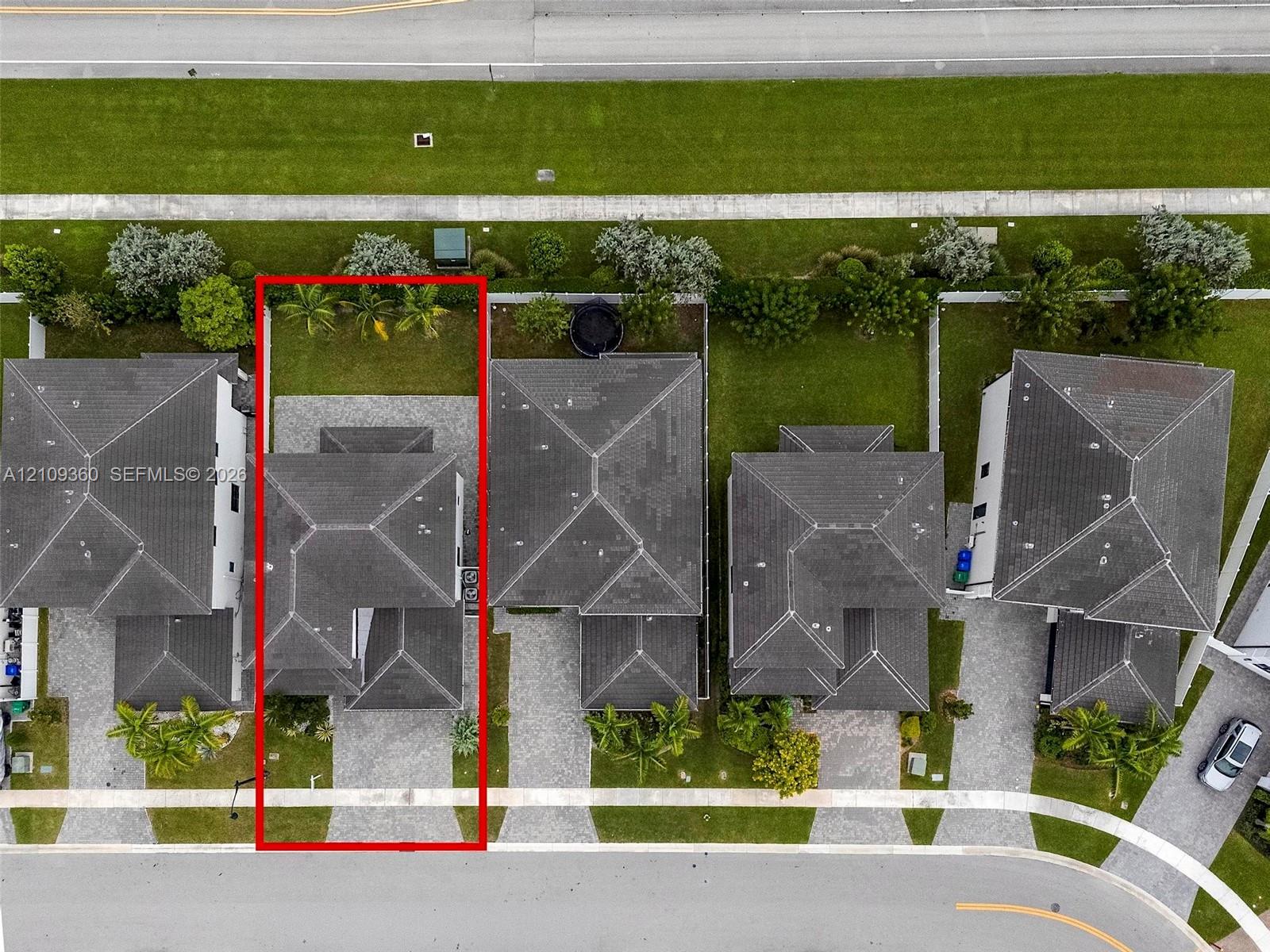 Aerial view of a residential property featuring a dark-toned hipped roof, paver driveway, and rear lawn area