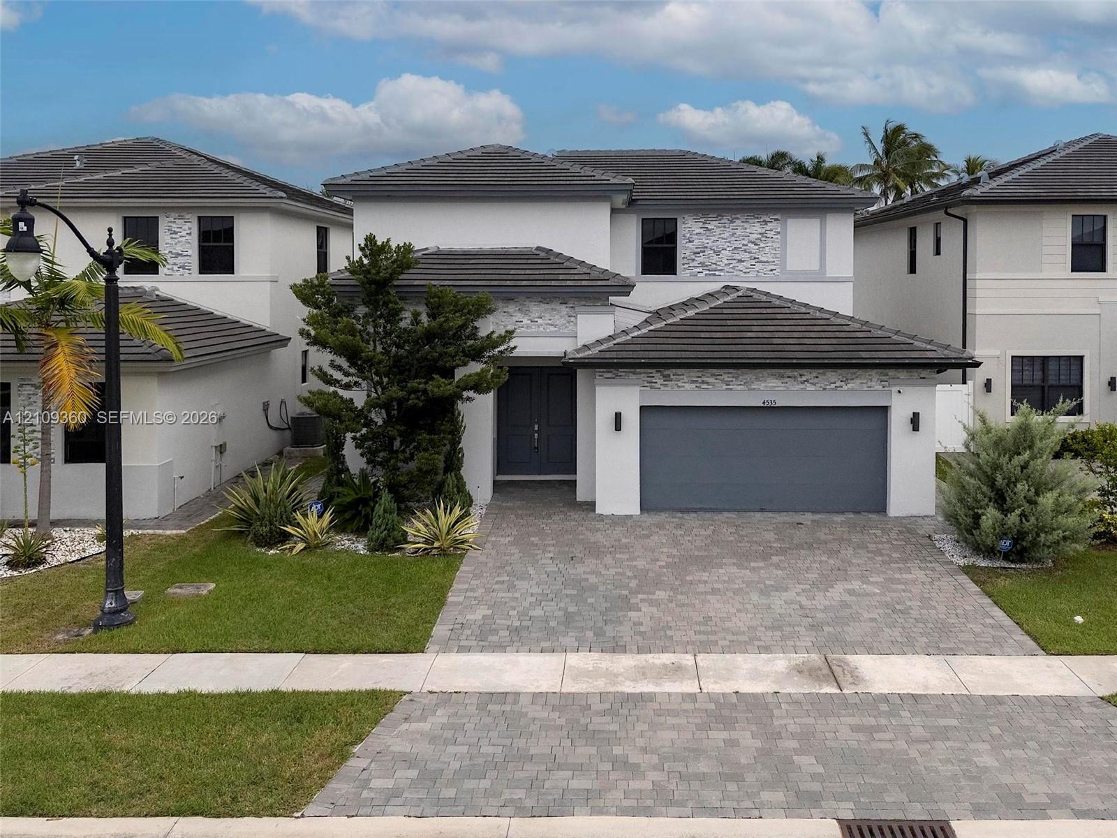 Two-story exterior featuring a tile roof, decorative stone accents, a multi-car garage, and a paved stone driveway