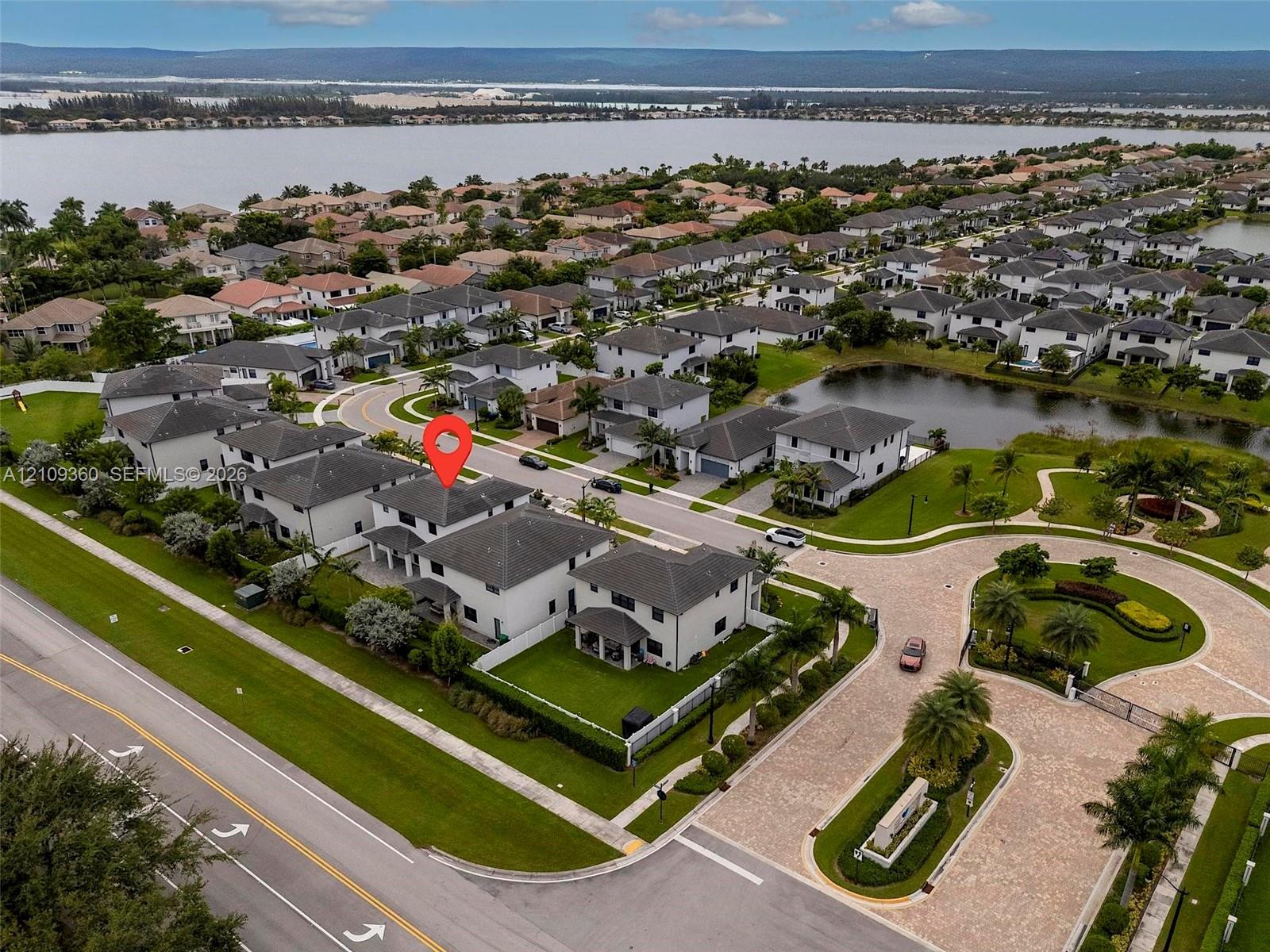 Aerial perspective of residential property featuring a multi-story exterior, attached garage, fenced perimeter, and proximity to expansive water frontage