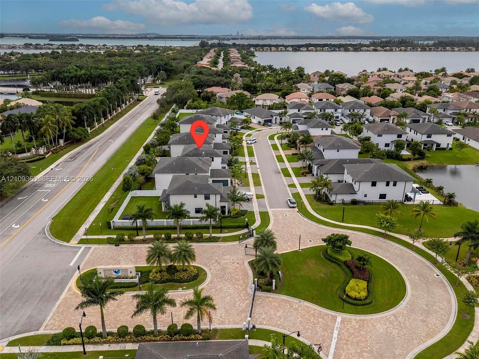 Aerial perspective of a multi-story residence situated within a gated community, featuring paver-stone common areas, mature palm landscaping, and proximity to expansive waterfront scenery