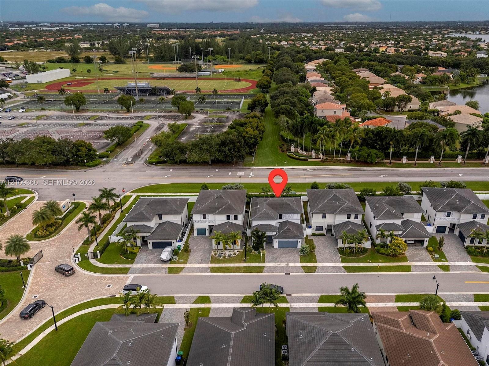 Aerial perspective of a two-story residence featuring a multi-pitched roof, attached garage, paved driveway, and established community landscaping