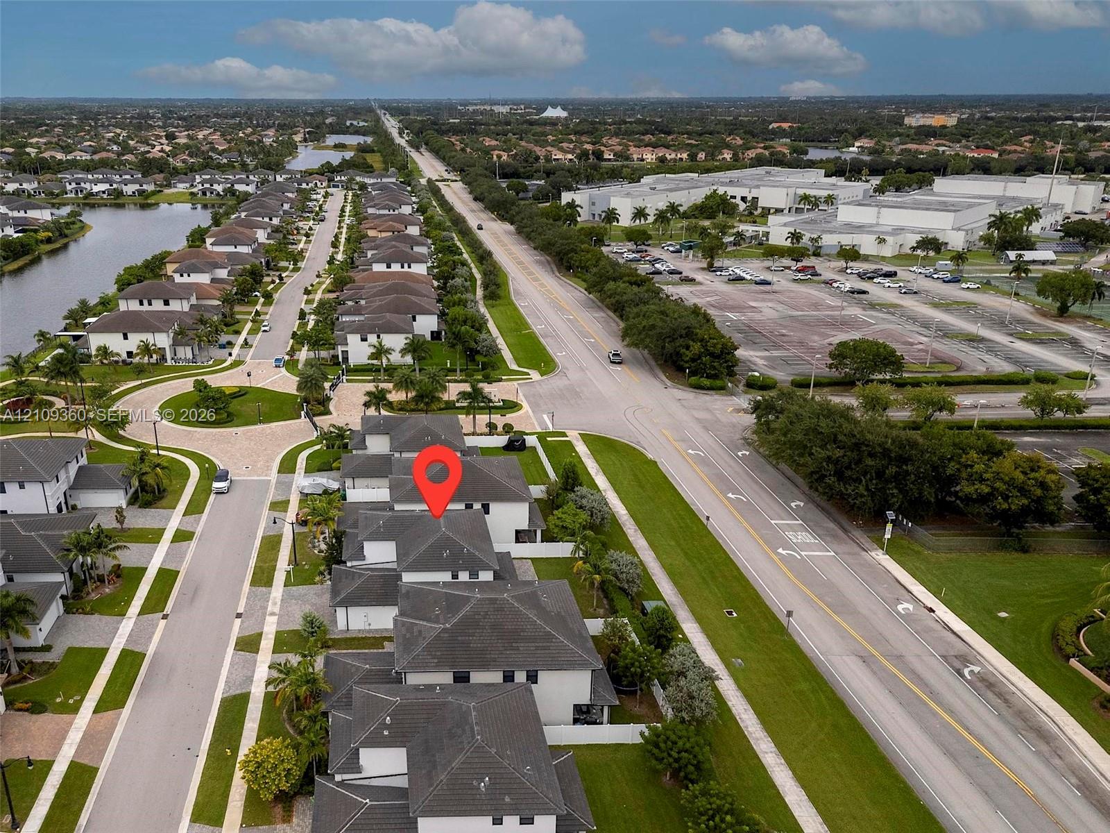 Aerial perspective of a multi-structure residential complex featuring multi-pitch shingled roofing, paved streets, manicured lawn areas, and native landscaping