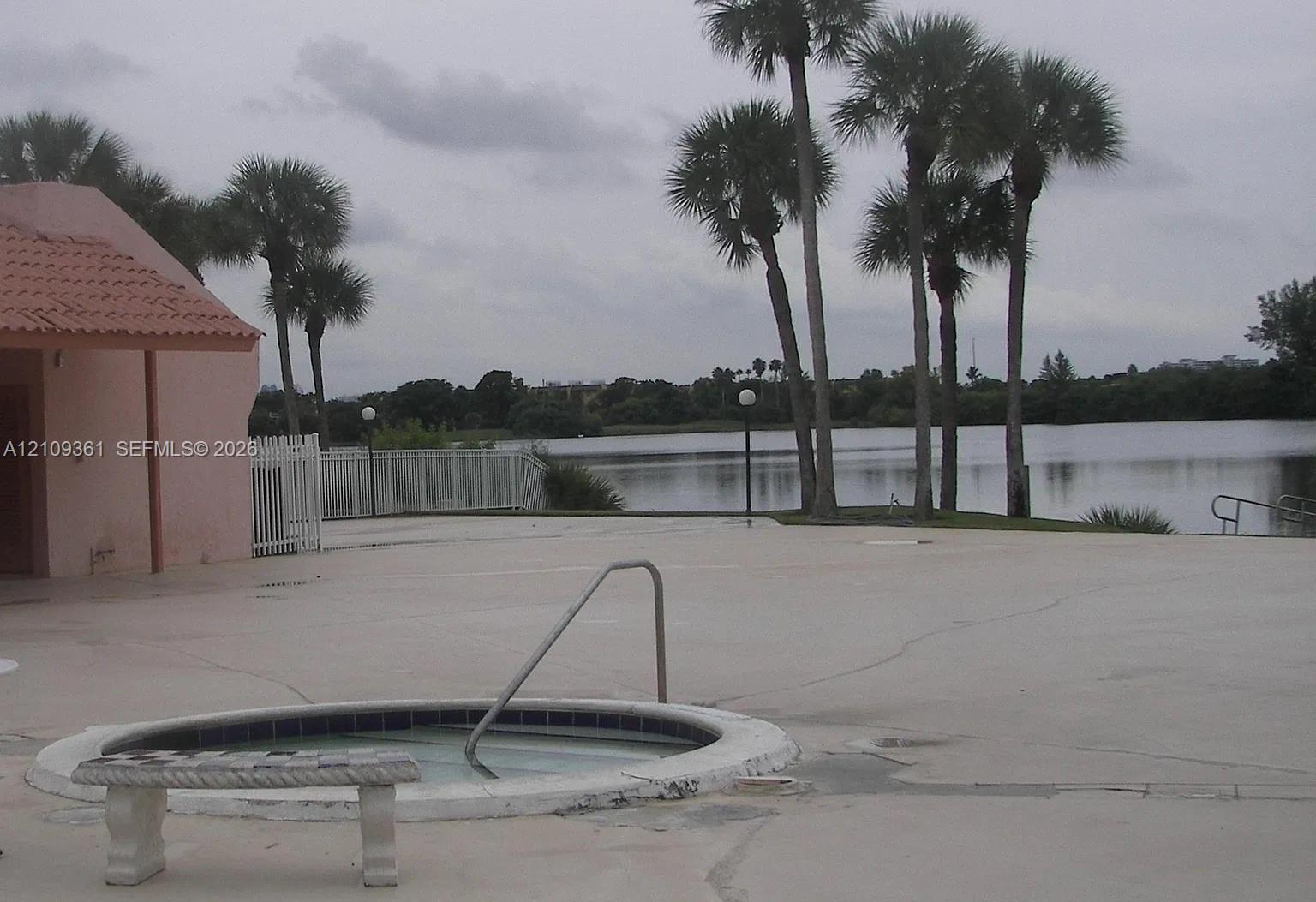 Circular inground spa with a metal handrail, concrete deck, and perimeter white fencing situated on a waterfront lot with mature palm trees Circular inground spa with a metal handrail, concrete deck, and perimeter white fencing situated on a waterfront lot with mature palm trees