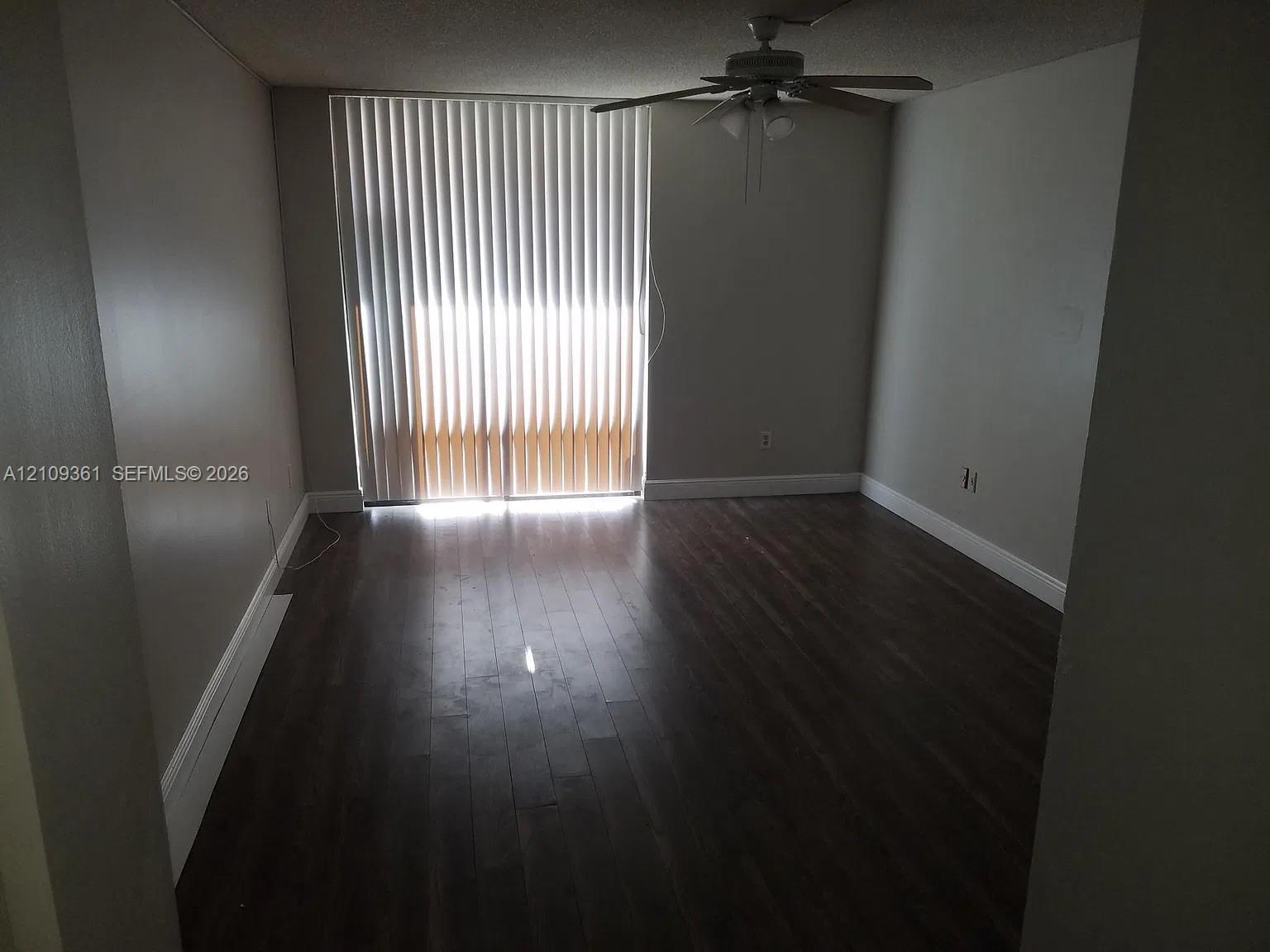 Interior space featuring wood-finish flooring, floor-to-ceiling vertical blinds, and a ceiling fan with integrated lighting