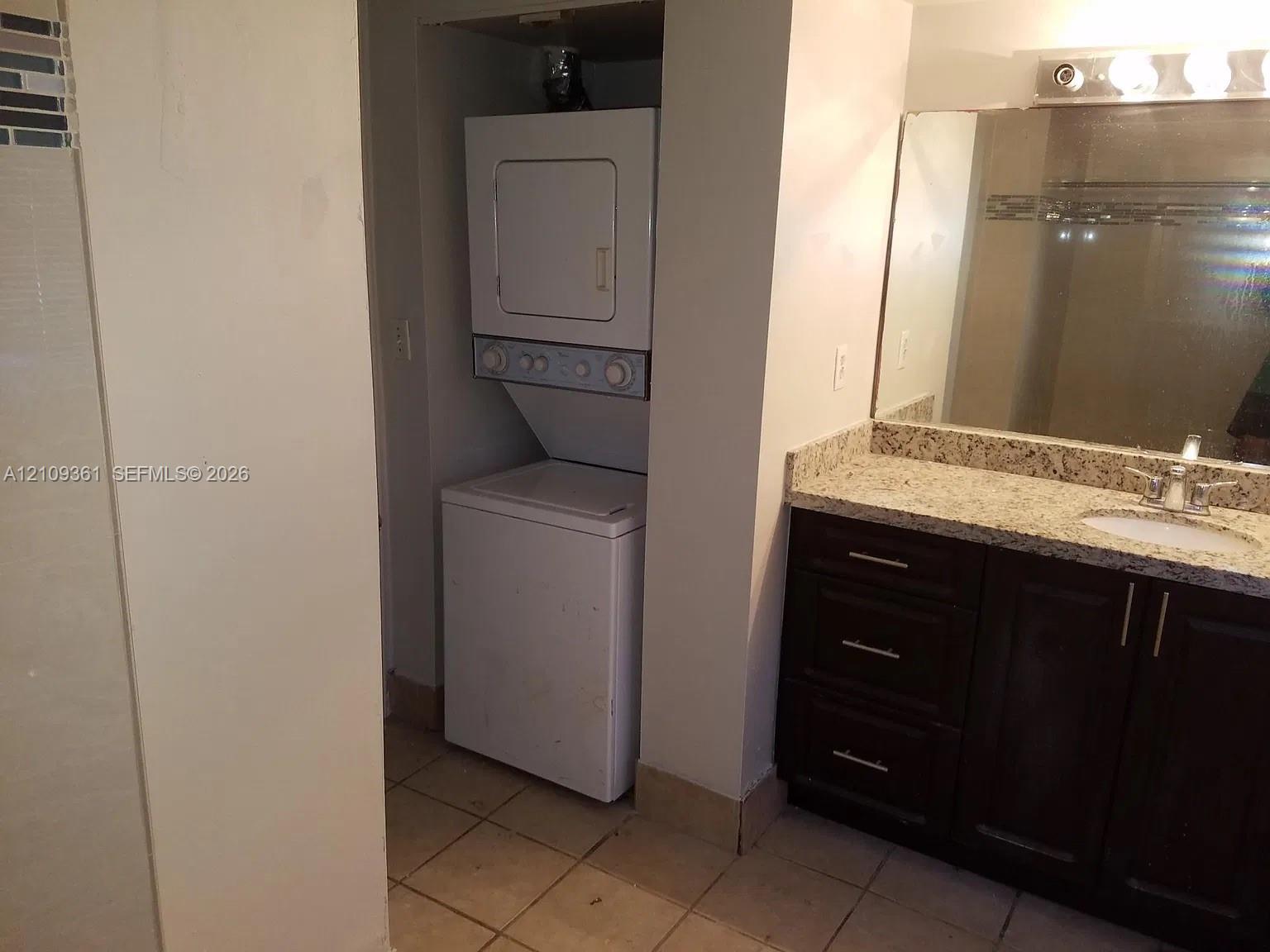 Stacked washer and dryer, vanity featuring stone-composite countertop, undermount sink, dark-finish cabinetry with metallic hardware, and full-width mirror Stacked washer and dryer, vanity featuring stone-composite countertop, undermount sink, dark-finish cabinetry with metallic hardware, and full-width mirror