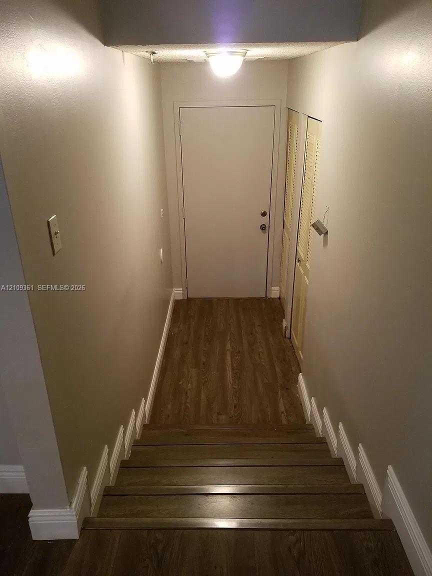 Staircase featuring wood-finish flooring, neutral wall paint, and dual louvered-door closet storage
