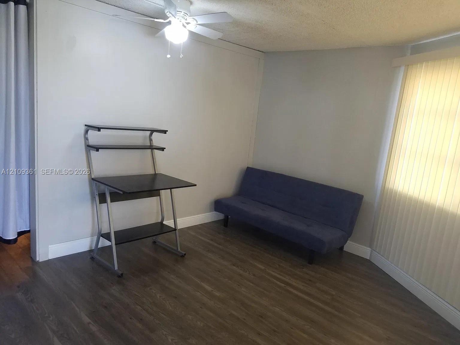Room featuring wood-finish flooring, a ceiling-mounted light fixture with a fan, and vertical window blinds