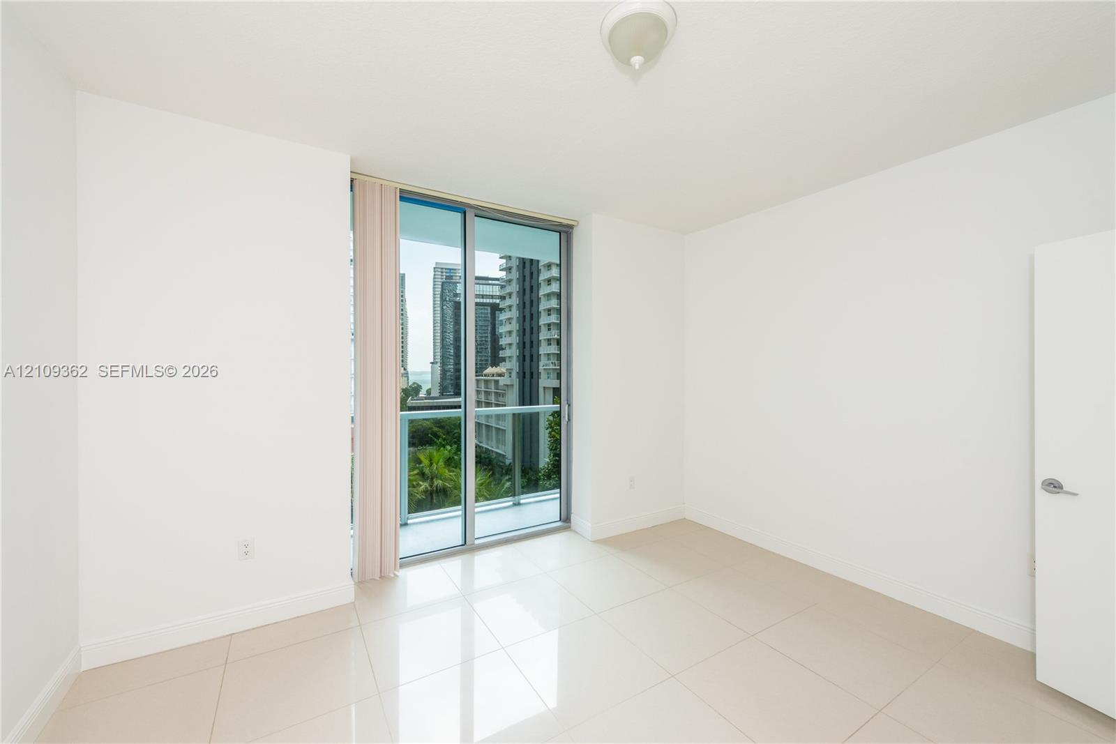 Neutral interior space featuring polished tile flooring, glass sliding balcony doors, and a ceiling-mounted light fixture