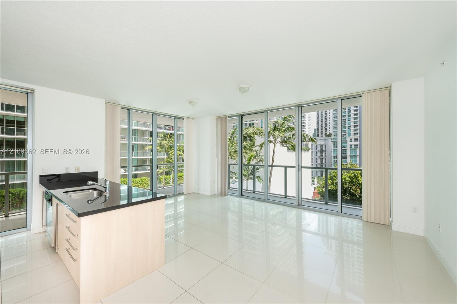 Open-concept space featuring floor-to-ceiling glass windows, polished tile flooring, and a kitchen island with dark stone countertops and light wood-finish cabinetry