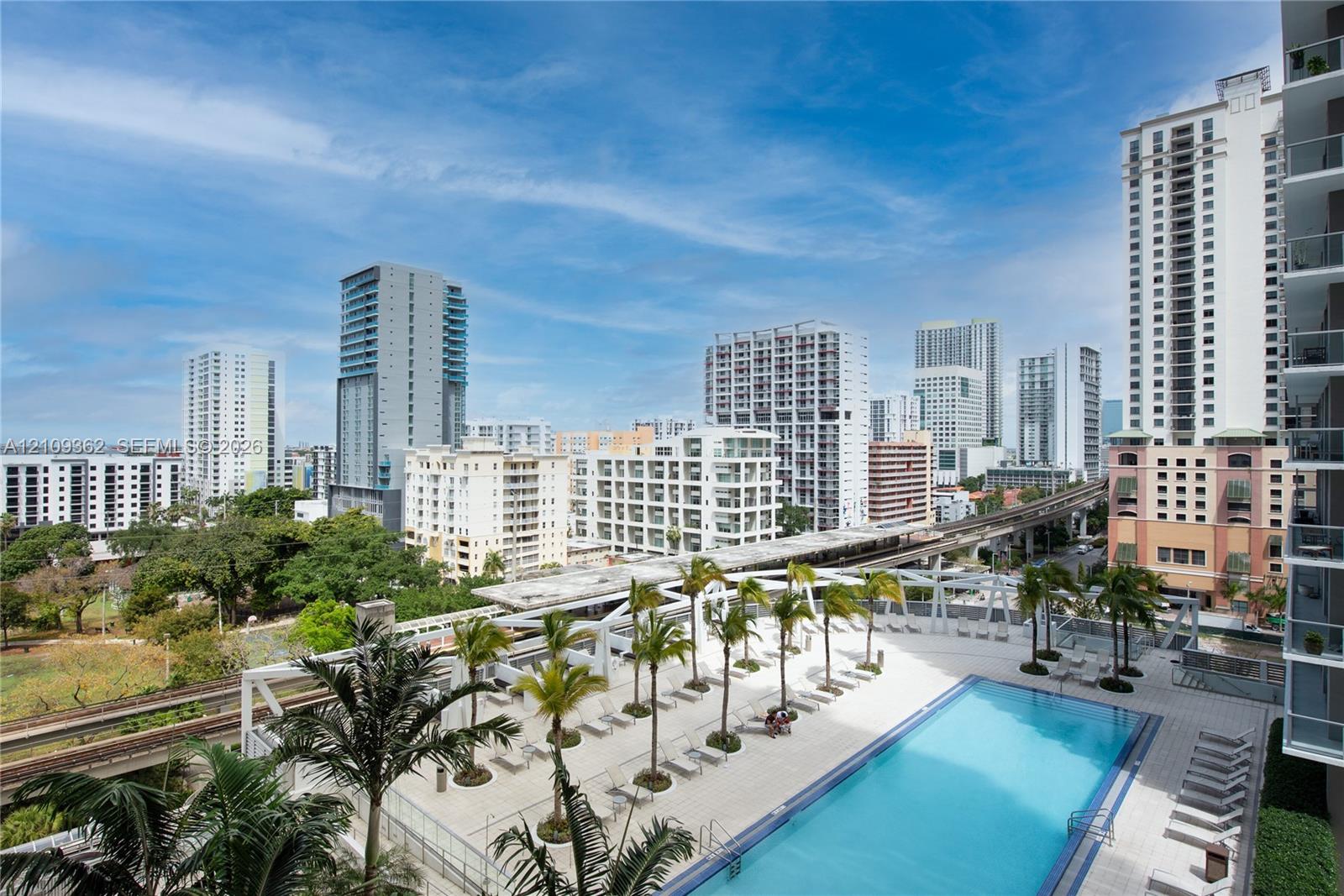 Outdoor swimming pool featuring a paved deck, glass railing enclosure, and mature palm tree landscaping