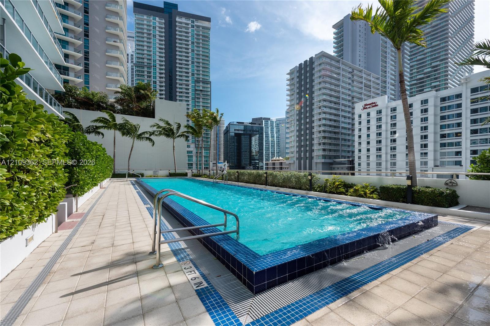 Elevated swimming pool featuring a tiled infinity edge, stainless steel grab rails, and surrounding ceramic tile decking