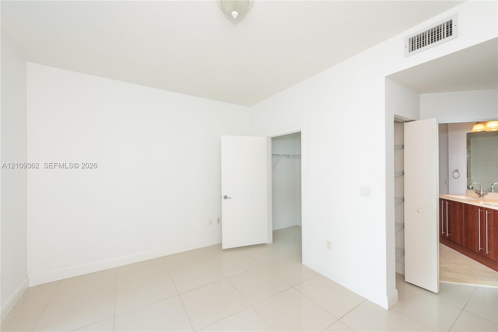 Neutral-toned tile flooring, walk-in closet with wire shelving, linen closet, and a bathroom featuring dark wood-finish cabinetry and a wide vanity mirror