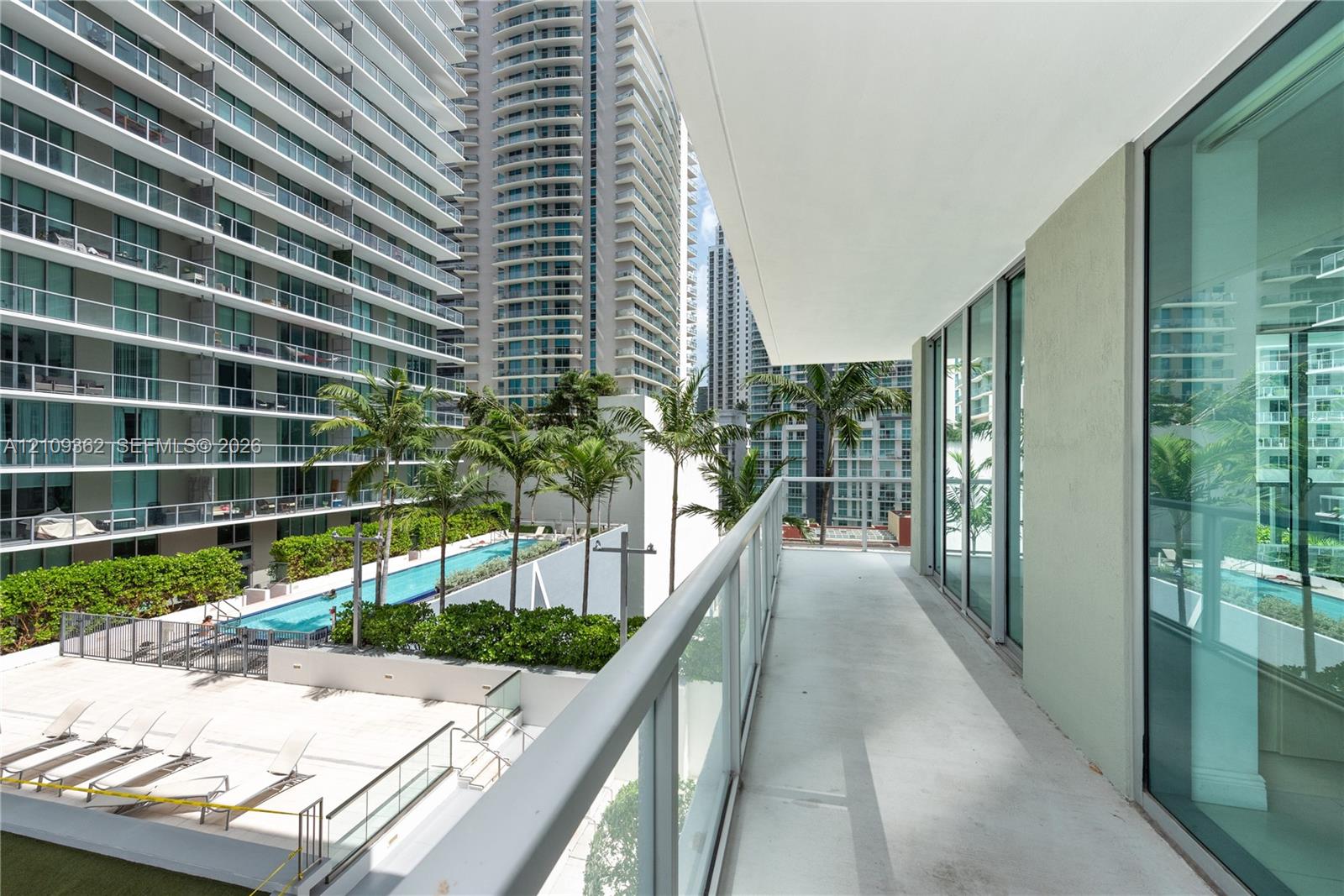 Covered balcony featuring a glass-panel railing, concrete flooring, and floor-to-ceiling glass wall