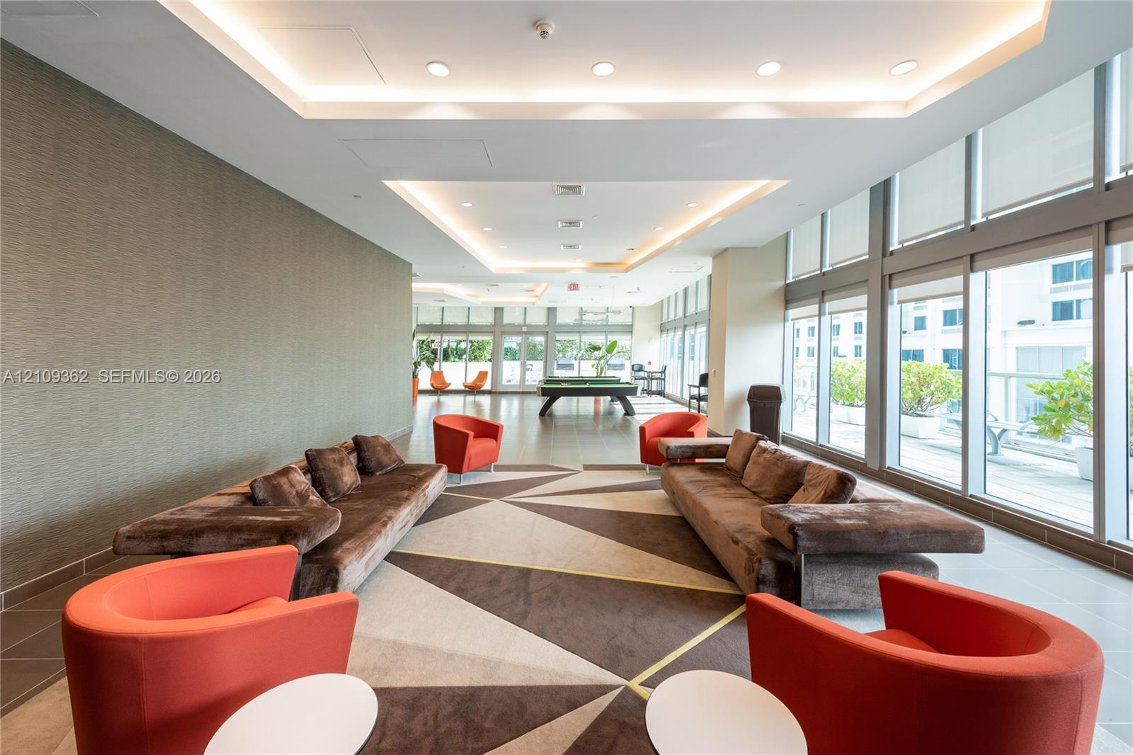 Common area featuring recessed tray ceilings with integrated lighting, floor-to-ceiling windows, and textured wall finish