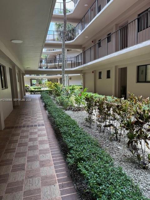 Multi-story exterior corridor featuring patterned paver flooring, dark metal railings, and a central landscaped courtyard with stone ground cover and mature foliage Multi-story exterior corridor featuring patterned paver flooring, dark metal railings, and a central landscaped courtyard with stone ground cover and mature foliage