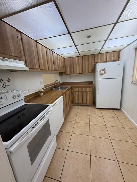 Kitchen featuring wood-finish cabinetry, solid surface countertops, ceramic tile flooring, and a dropped ceiling with integrated panel lighting Kitchen featuring wood-finish cabinetry, solid surface countertops, ceramic tile flooring, and a dropped ceiling with integrated panel lighting