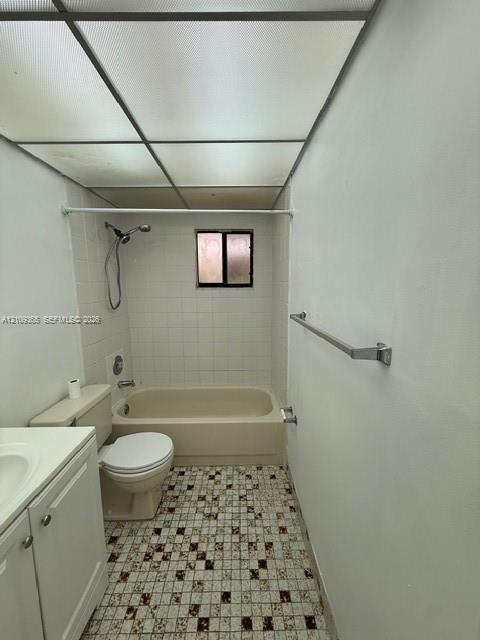 Bathroom featuring a drop-in bathtub with a wall-mounted showerhead, white tile tub surround, patterned mosaic floor tile, and a built-in white vanity Bathroom featuring a drop-in bathtub with a wall-mounted showerhead, white tile tub surround, patterned mosaic floor tile, and a built-in white vanity