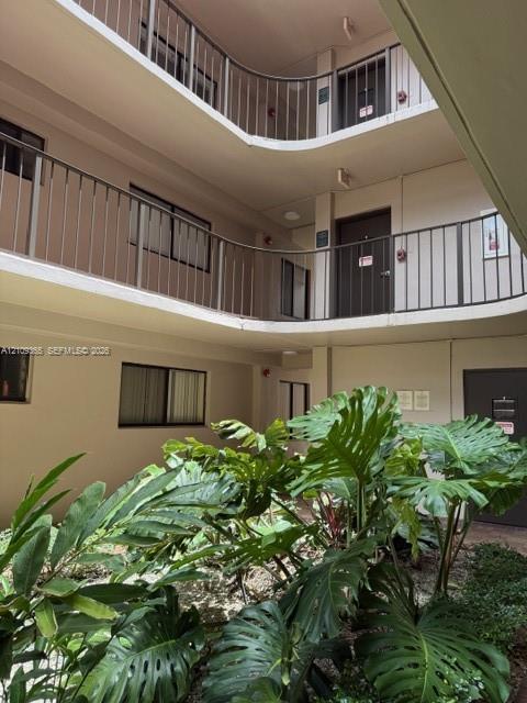 Exterior courtyard featuring multi-level walkways with metal railings, neutral-tone siding, and mature tropical greenery within a landscaped garden bed Exterior courtyard featuring multi-level walkways with metal railings, neutral-tone siding, and mature tropical greenery within a landscaped garden bed