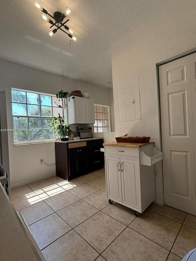 Multi-tone cabinetry featuring white upper cabinets and dark lower cabinetry, ceramic tile flooring, multi-pane window, and an industrial-style multi-arm ceiling light fixture