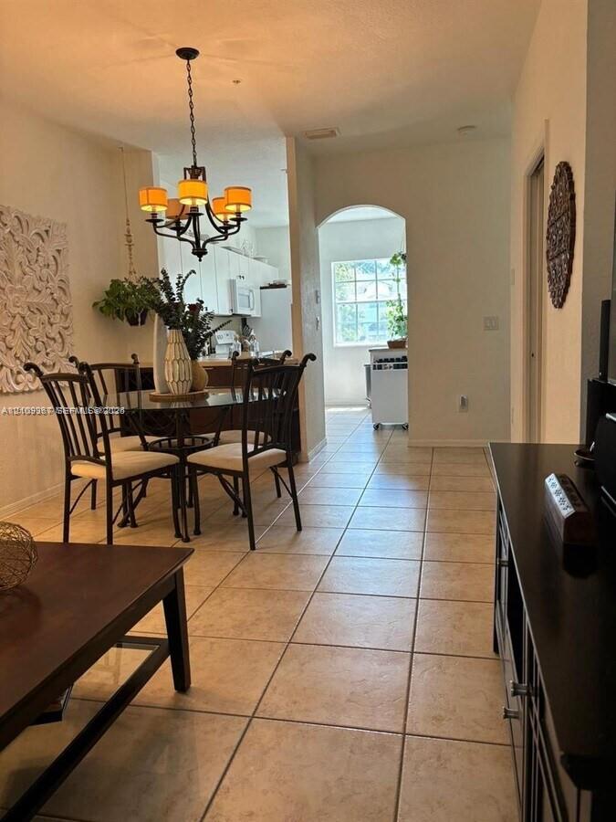 Ceramic tile flooring, multi-light hanging chandelier, and arched doorway entry