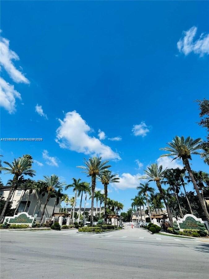 Gated entrance featuring decorative stone signage, established palm tree landscaping, and paved roadway Gated entrance featuring decorative stone signage, established palm tree landscaping, and paved roadway