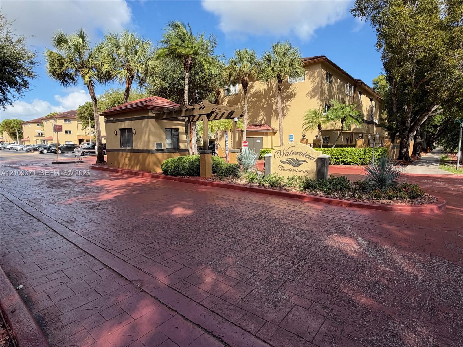 Gated entrance featuring a stamped concrete drive, an attended guard house, and mature palm landscaping