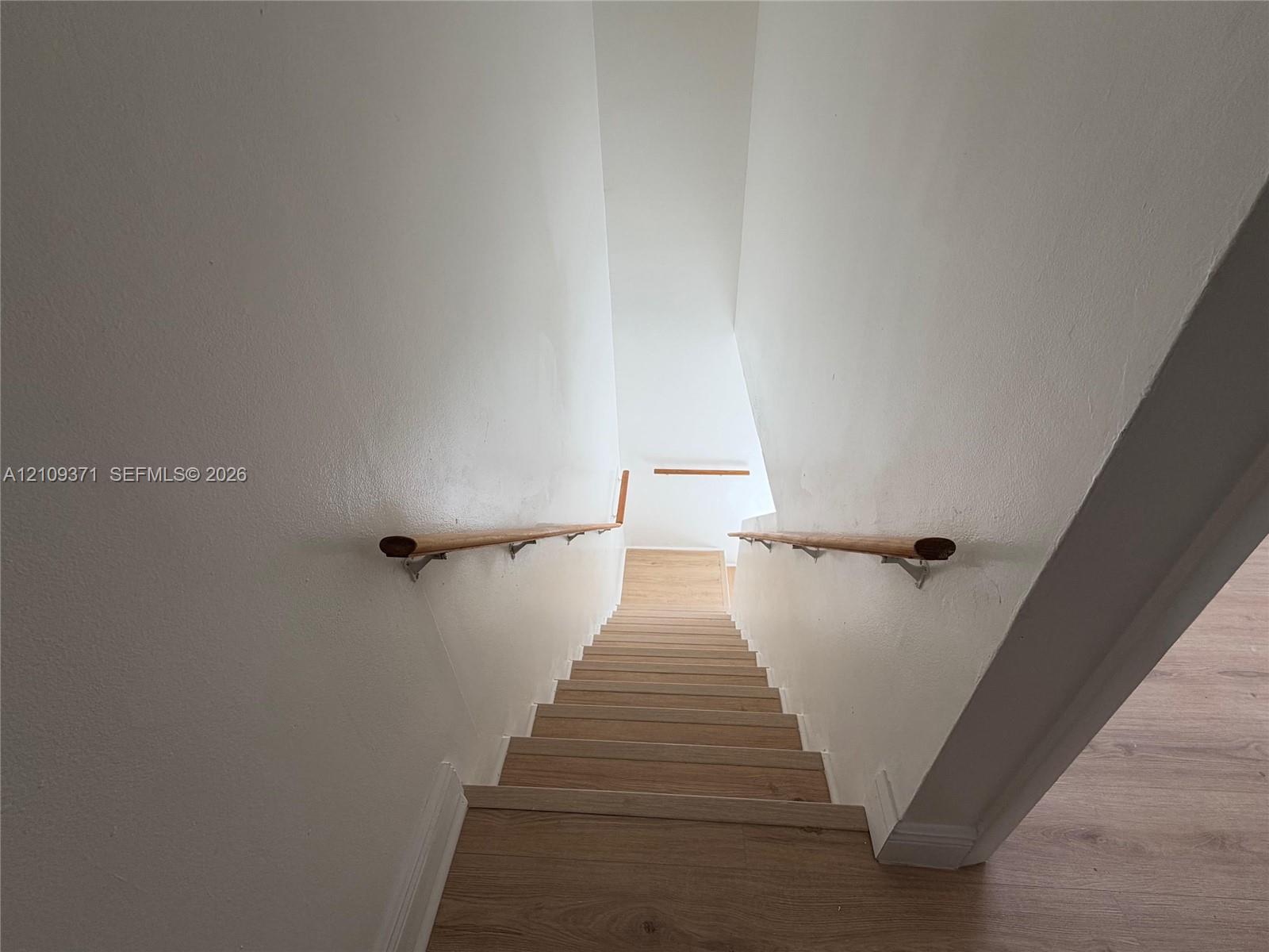 Staircase featuring wood-finish flooring and dual wooden handrails with metal brackets