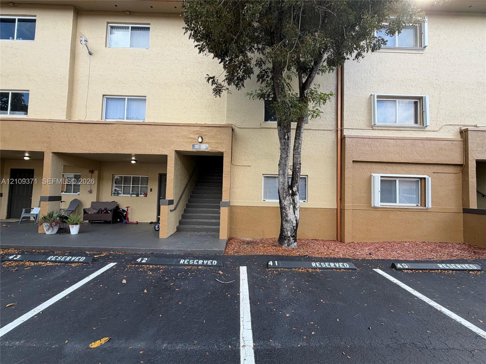 Multi-story exterior featuring a textured stucco facade, covered ground-level patio, exterior staircase, and dedicated reserved parking spaces