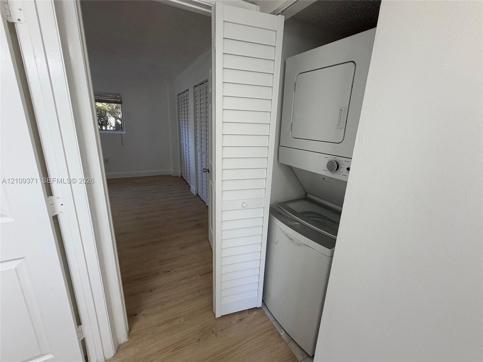 Stacked laundry unit enclosed by white louvered doors, featuring wood-finish flooring and paneled interior doors