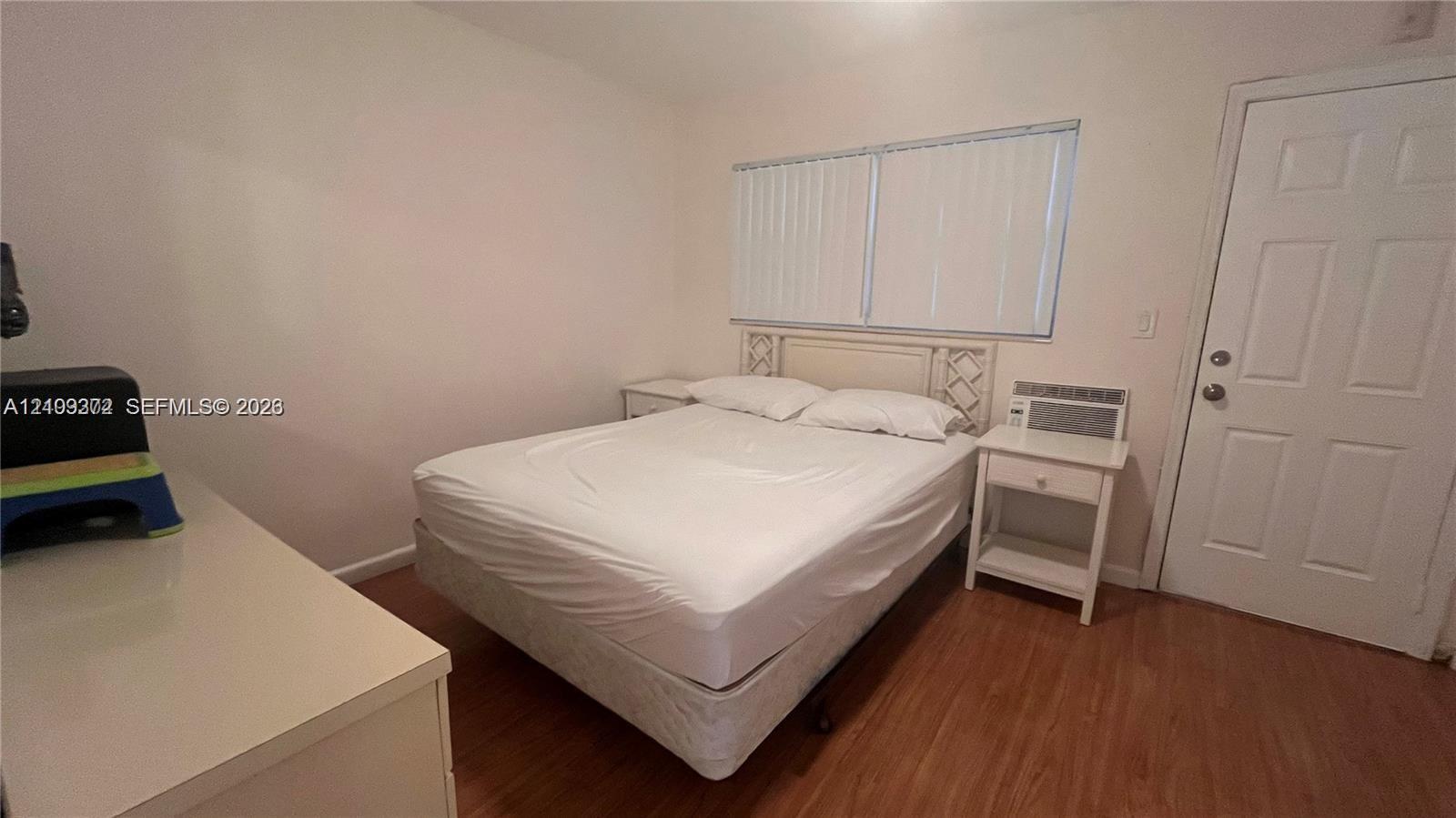 Interior room featuring wood-finish flooring, a six-panel door, and dual-pane windows with integrated blinds