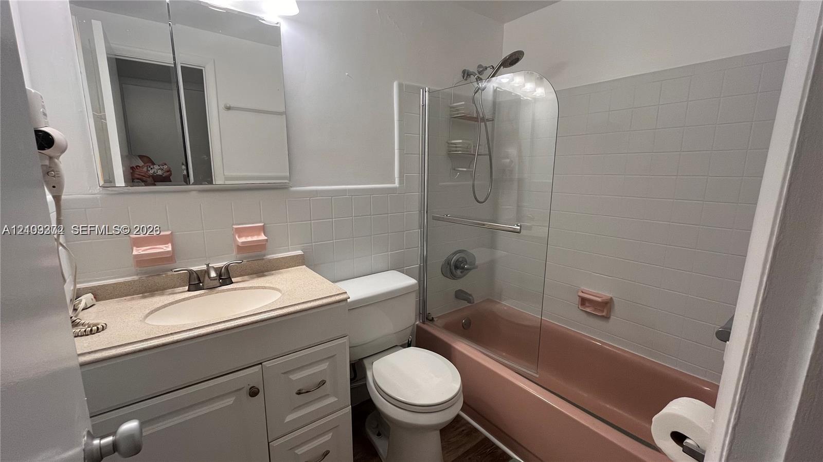 Bathroom featuring a vanity cabinet, integrated sink, mirrored medicine cabinet, and a bathtub with a glass panel enclosure and wall-mounted shower fixture