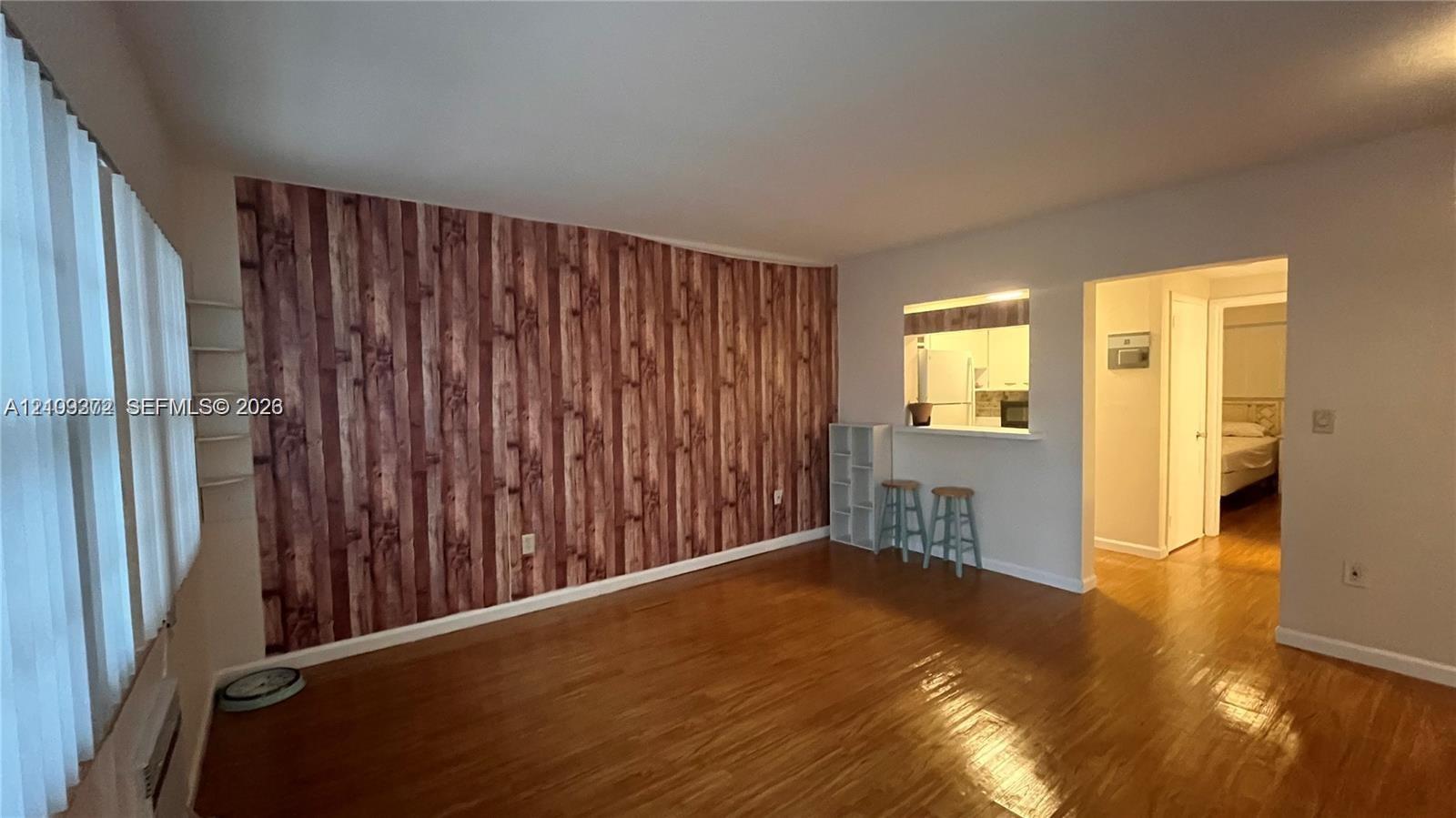 Interior space featuring wood-finish flooring, a wood-paneled accent wall, and a passthrough opening to the kitchen