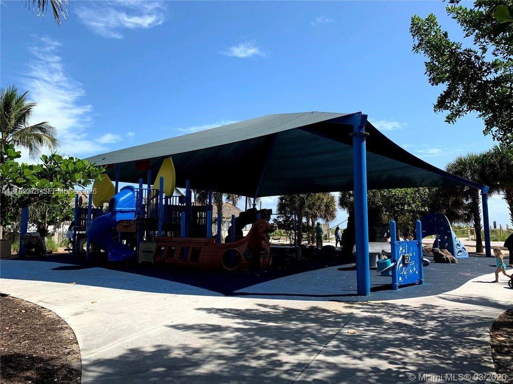 Recreational area featuring a large fabric shade structure, integrated play equipment, and a paved walkway surface
