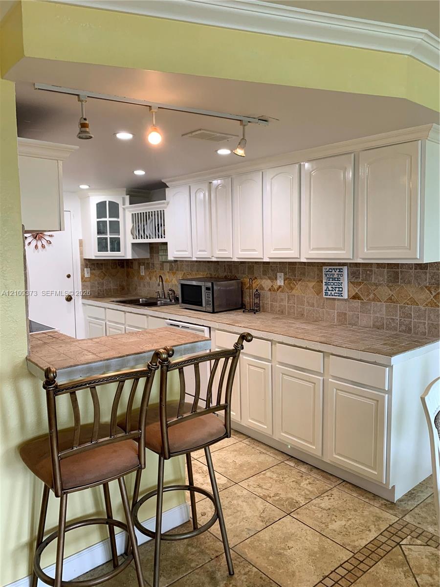 Kitchen featuring white cabinetry, tile countertops, tile backsplash, tile flooring, and adjustable track lighting