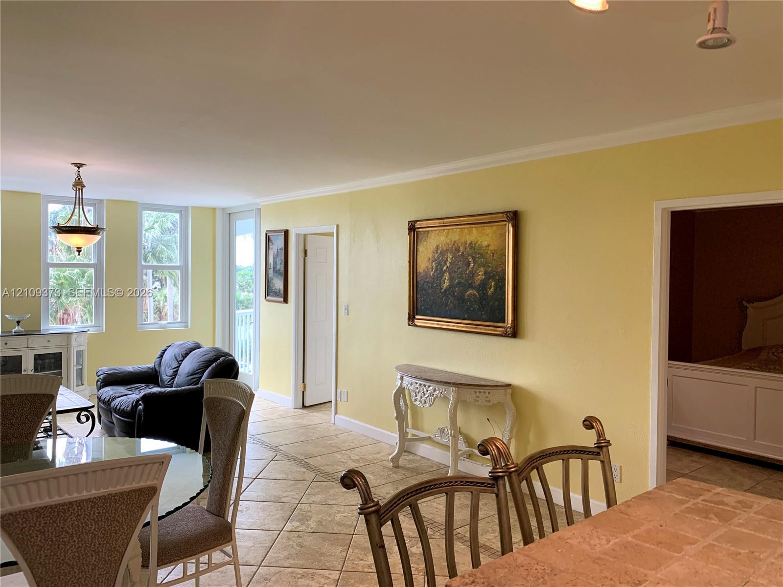 Open living space featuring tile flooring, multi-pane windows, a hanging pendant light fixture, and crown molding