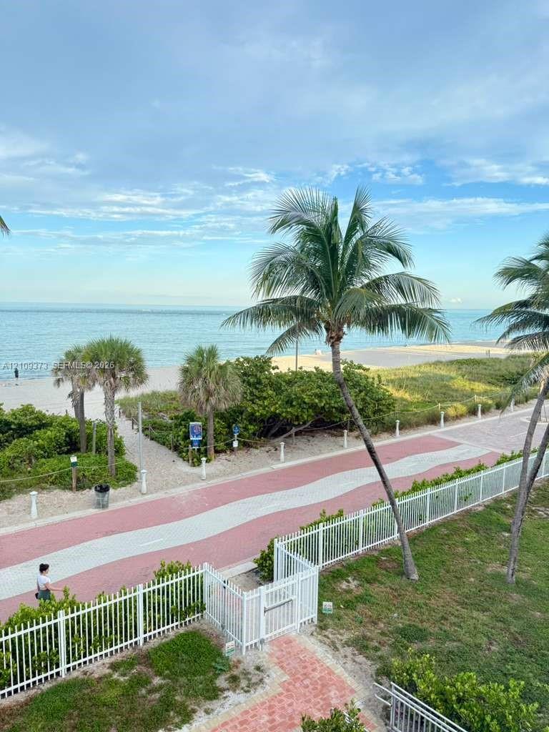 Coastal property featuring a white metal perimeter fence, gated access, manicured landscaping, and mature palm trees with direct ocean and beach exposure