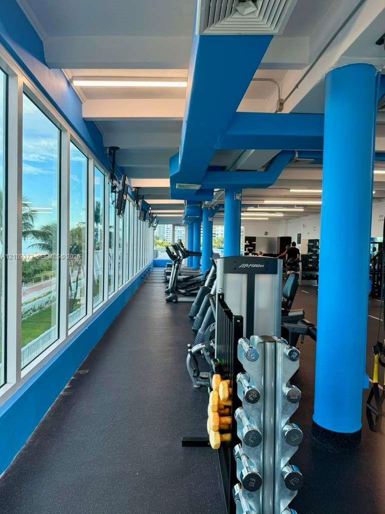 Fitness area featuring floor-to-ceiling windows, rubberized flooring, exposed structural pillars, and recessed lighting