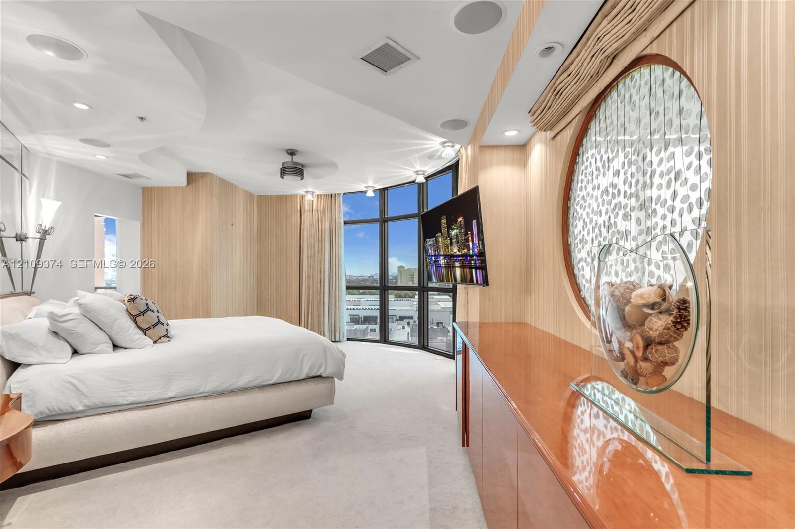 Floor-to-ceiling windows with panoramic exterior exposure, curved architectural ceiling detail, built-in cabinetry with high-gloss finish, circular wall accent, and integrated audio speakers