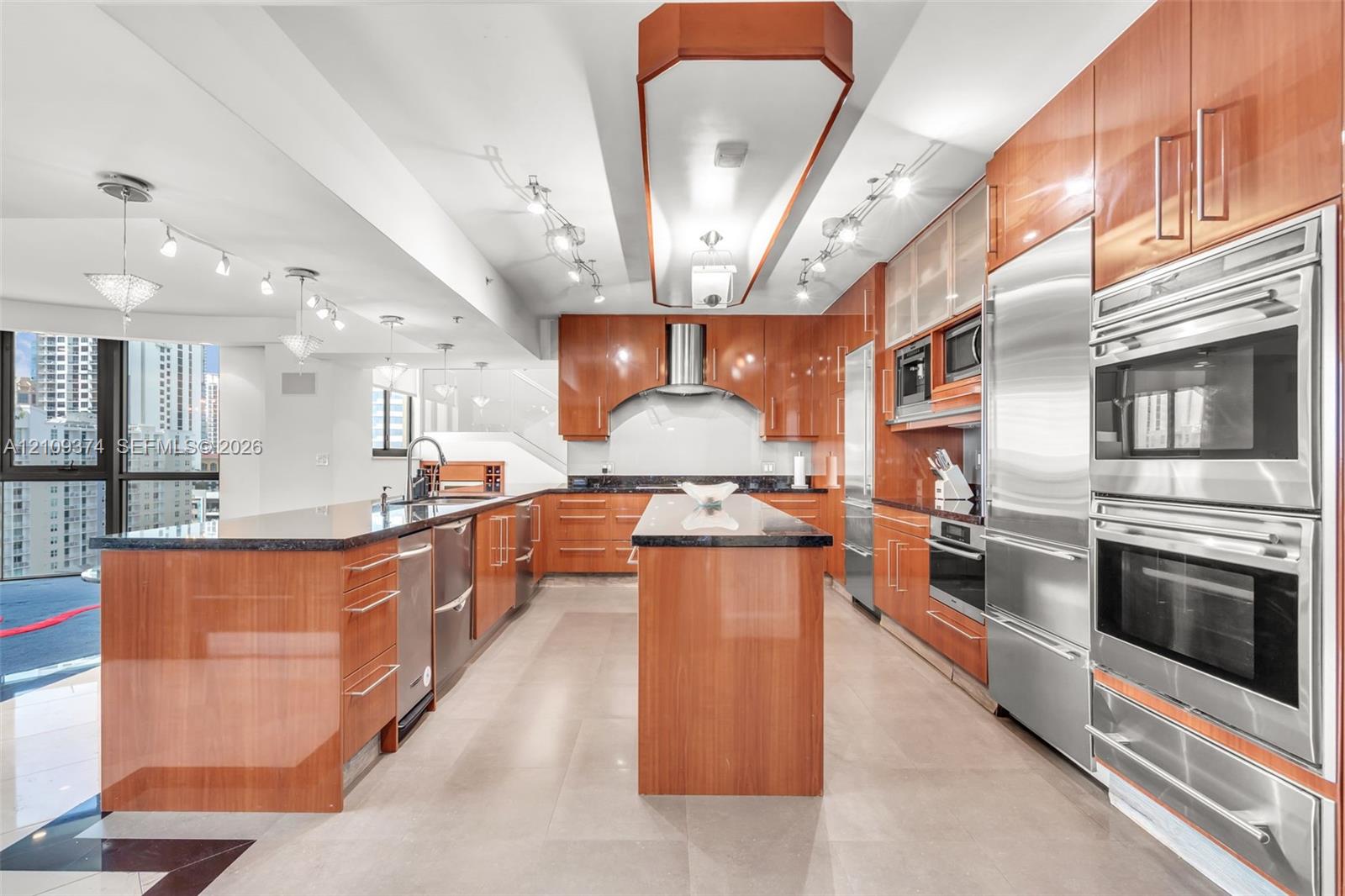 Contemporary kitchen featuring high-gloss cabinetry, stone countertops, double wall ovens, integrated stainless steel refrigeration, and a central island with a prep sink