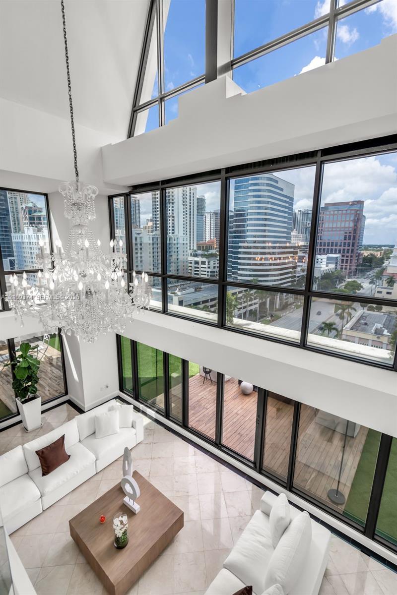 Double-height vaulted ceilings featuring floor-to-ceiling multi-story windows, polished stone flooring, intricate tiered crystal chandelier, and direct access to a wood-decked outdoor terrace