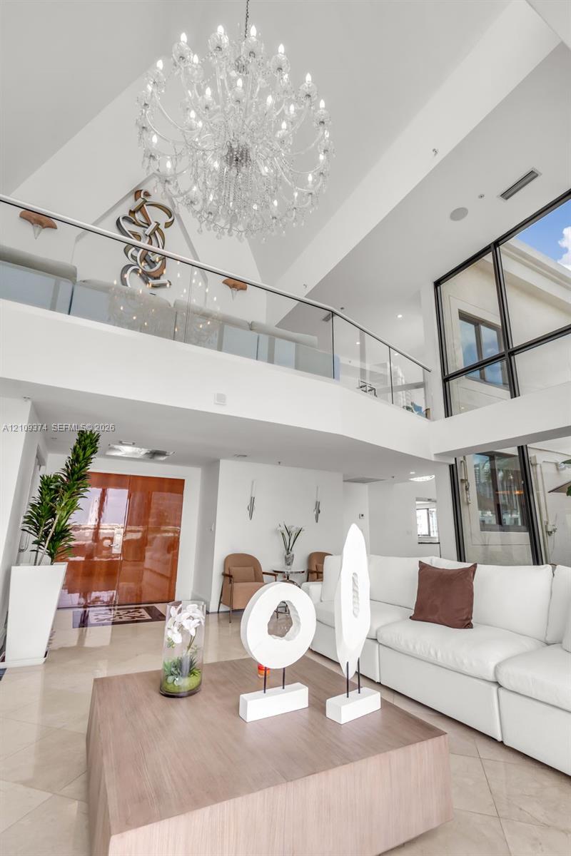 Two-story foyer featuring vaulted ceilings, floor-to-ceiling windows, a large multi-tiered crystal chandelier, and a glass-paneled mezzanine railing Two-story foyer featuring vaulted ceilings, floor-to-ceiling windows, a large multi-tiered crystal chandelier, and a glass-paneled mezzanine railing
