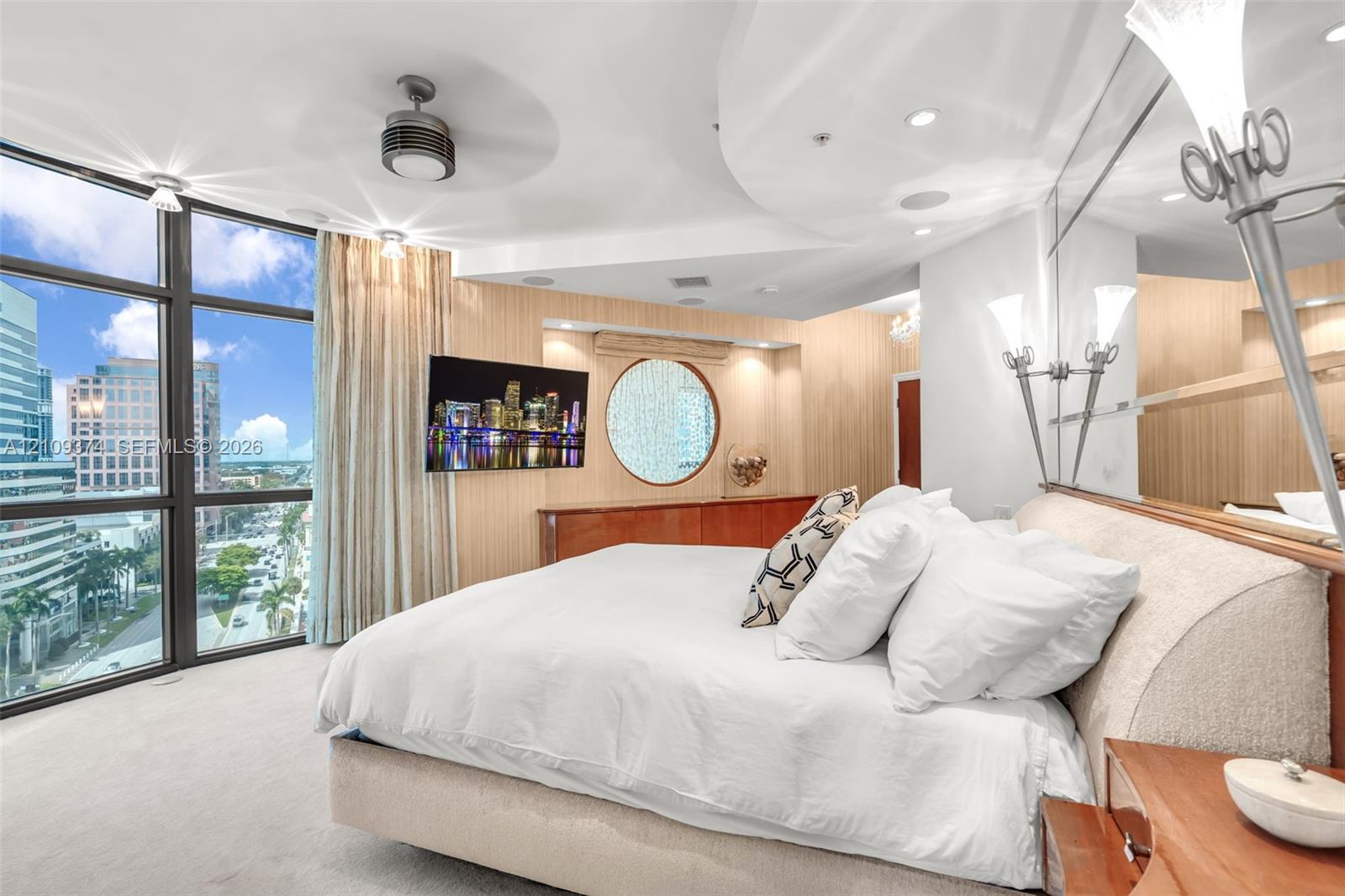 Floor-to-ceiling windows with urban scenery, custom wood-paneled wall accents, circular feature window, recessed ceiling lighting, and built-in wall-mounted cabinetry